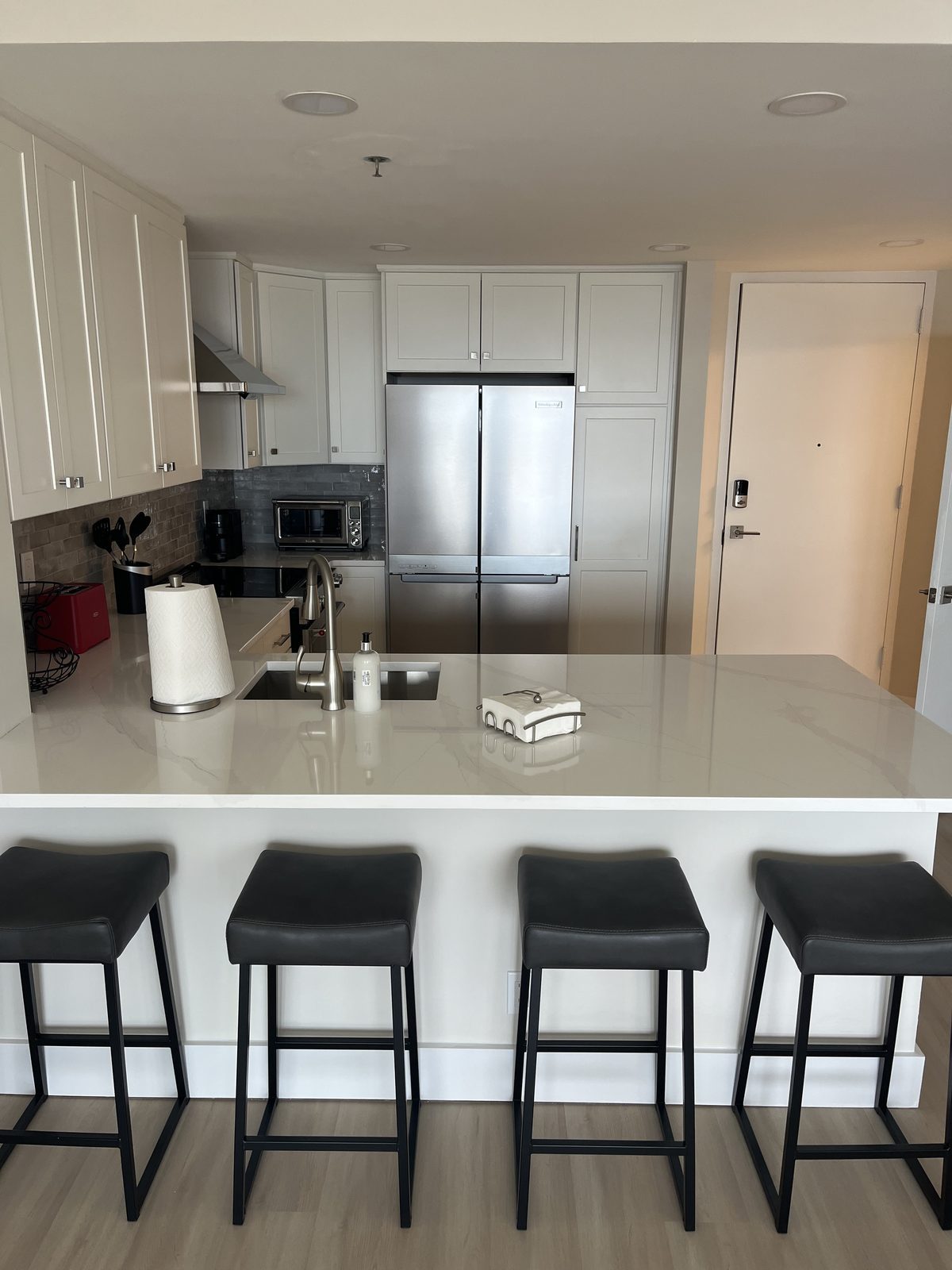 Condo kitchen with white cabinets, quartz counters and stainless refrigerator, remodeled by Boardwalk Renovations