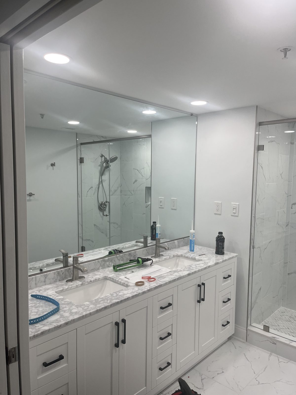 White double vanity with marble-look top beside a frameless glass shower, remodeled by Boardwalk Renovations