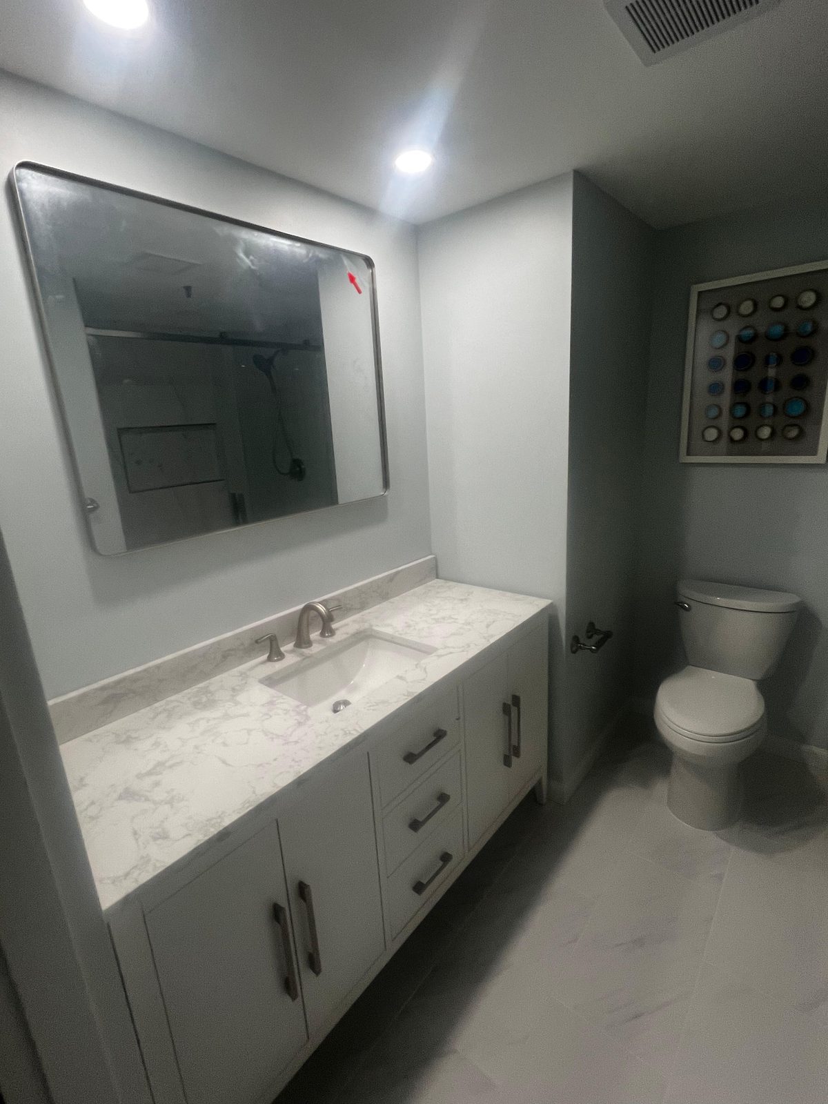 Gray shaker vanity with marble-look top and large frameless mirror, remodeled by Boardwalk Renovations